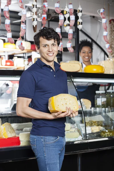 Hombre feliz sosteniendo queso en frente de la tienda de comestibles —  Fotos de Stock