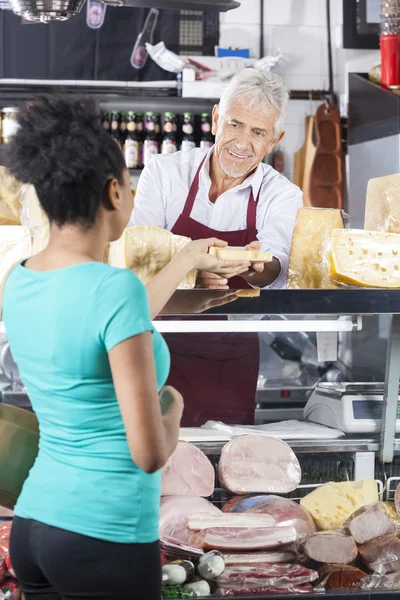 Vendedor sênior dando queijo ao cliente feminino — Fotografia de Stock