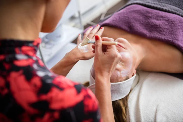 Esteticista aplicando mascarilla facial en cara de mujer —  Fotos de Stock