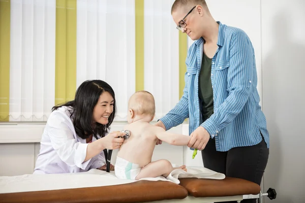 Mutter schaut lächelnden Kinderarzt an, der Baby im Bett untersucht — Stockfoto