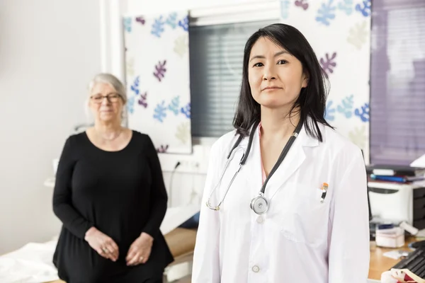 Medico fiducioso in piedi mentre paziente seduto in background — Foto Stock