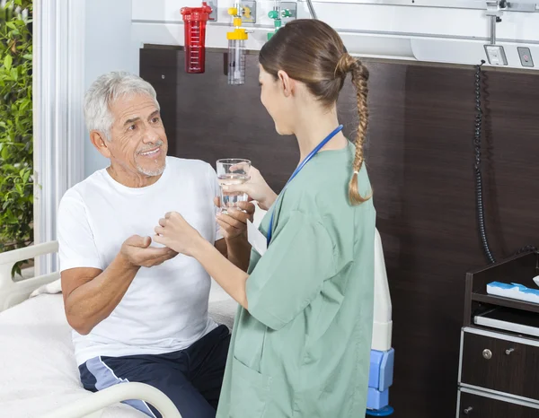 Счастливый пациент получает лекарства и стакан воды от медсестры — стоковое фото