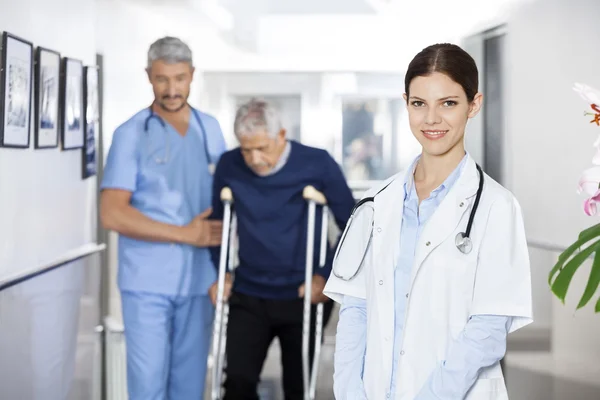 Läkare leende medan kollega bistå äldre Man med Crutche — Stockfoto