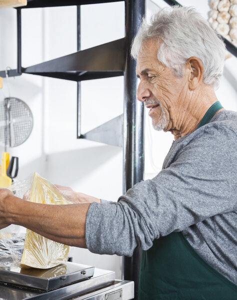 Senior Salesman Packing Cheese At Grocery Store