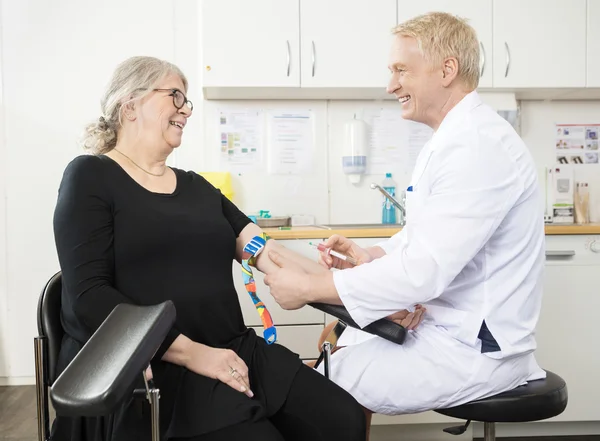 Medico sorridente che raccoglie il sangue dei pazienti anziani per il test in Cli — Foto Stock