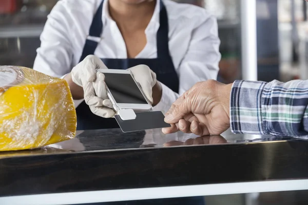 Vendedora aceita pagamento do cliente na loja de queijos — Fotografia de Stock