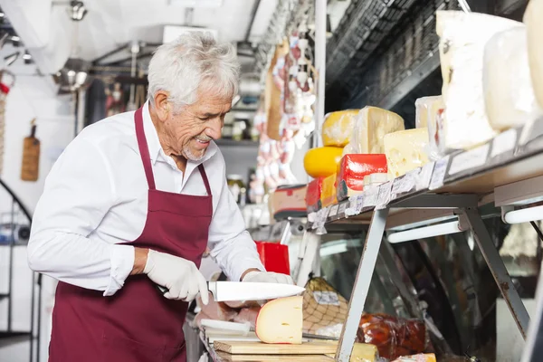 Glücklicher Verkäufer schneidet Käse im Geschäft — Stockfoto