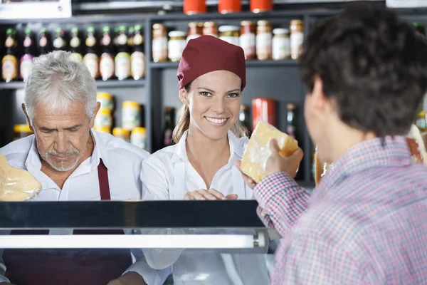 Vendedora sonriente sirviendo queso al cliente en la tienda — Foto de Stock