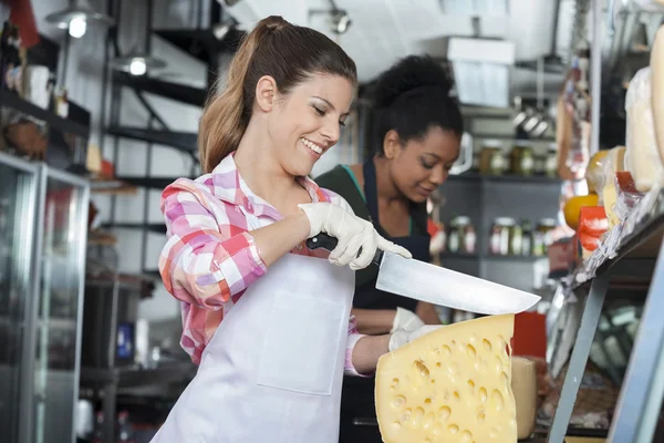 Felice giovane donna affettare formaggio con coltello in negozio — Foto Stock