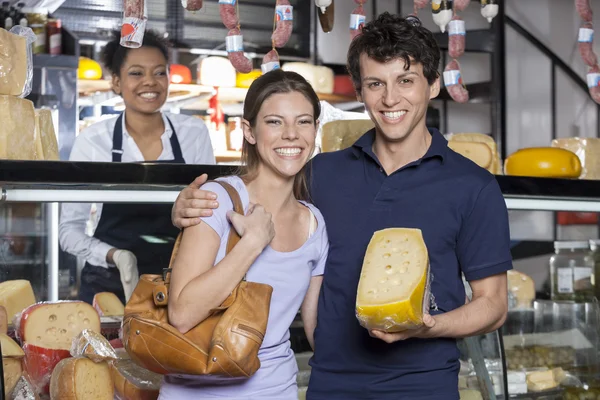 Jovem feliz casal segurando queijo na mercearia — Fotografia de Stock