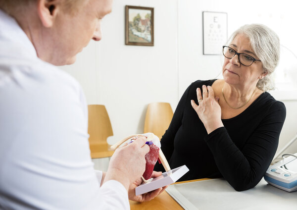 Woman Looking At Male Doctor Explaining Shoulder Rotator Cuff Mo