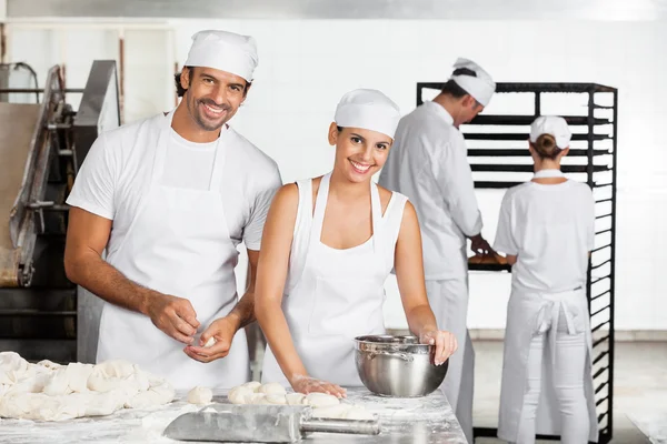 Panaderos sonrientes haciendo masa juntos en panadería — Foto de Stock