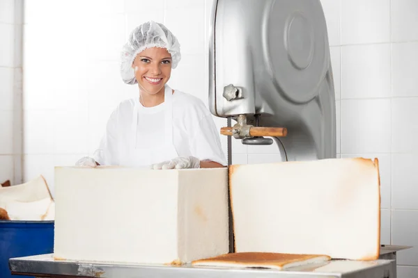 Boulanger femelle avec pain debout à la machine de découpe — Photo
