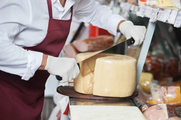 Försäljaren skivning ost med dubbel hanteras kniv — Stockfoto