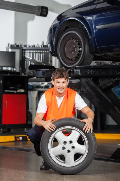Feliz mecánico sosteniendo neumático en taller de reparación —  Fotos de Stock