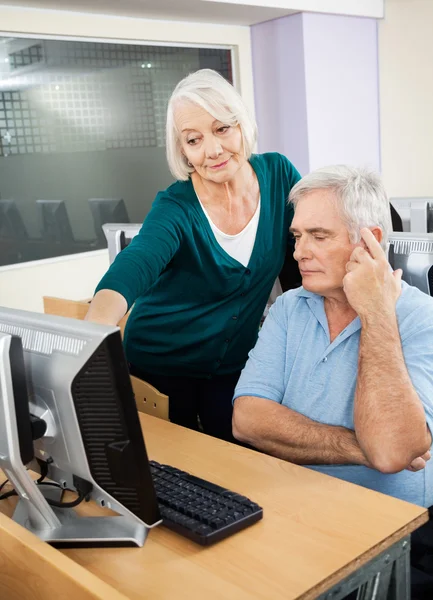 Donna che assiste compagno di classe maschile nel laboratorio di informatica — Foto Stock