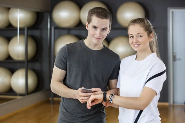 Jóvenes amigos usando teléfono inteligente y podómetro en el gimnasio —  Fotos de Stock