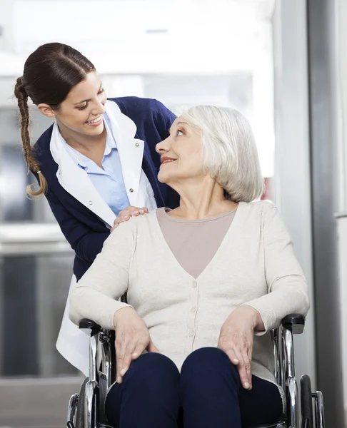 Физиотерапевт смотрит на старшего пациента, сидящего в инвалидном кресле — стоковое фото