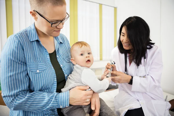 Baby grijpen Otoscoop vanuit dokter zittend op moeders schoot — Stockfoto