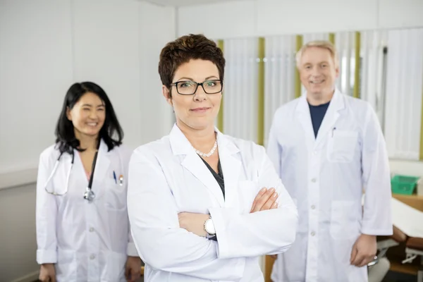 Doctor staande armen gekruist terwijl collega's glimlachend In kliniek — Stockfoto