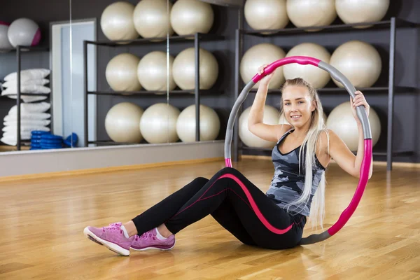 Donna che tiene il cerchio mentre si siede sul pavimento in palestra — Foto Stock