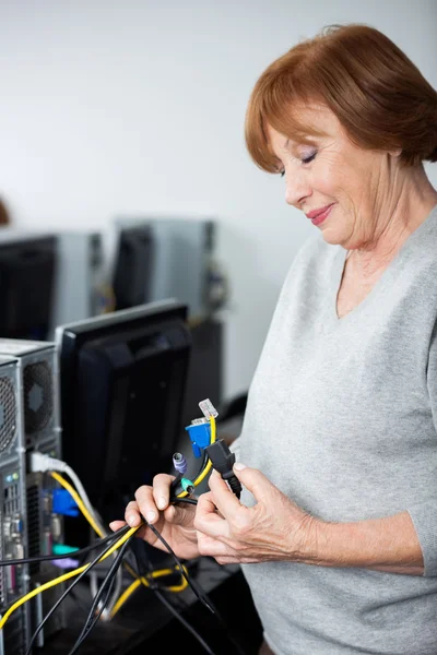 Старшая женщина, наблюдающая за компьютерными кабелями — стоковое фото