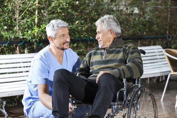 Fisioterapeuta masculino mirando a un hombre mayor discapacitado en Wheelchai —  Fotos de Stock