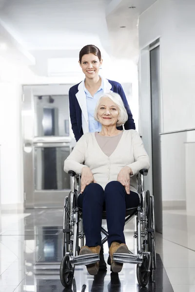 Улыбающийся физиотерапевт толкает пожилую женщину в инвалидное кресло — стоковое фото