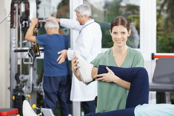 Fizjoterapeuta pomaga pacjenta z nogi ćwiczenia w Fitness Cen — Zdjęcie stockowe