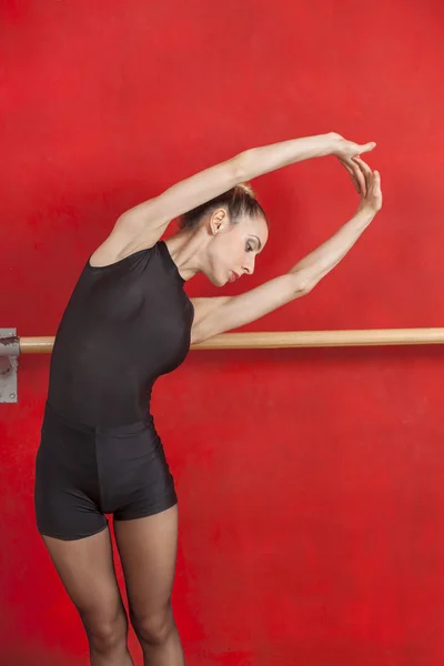 Ballerina Stretching With Arms Raised against Red Wall — стоковое фото