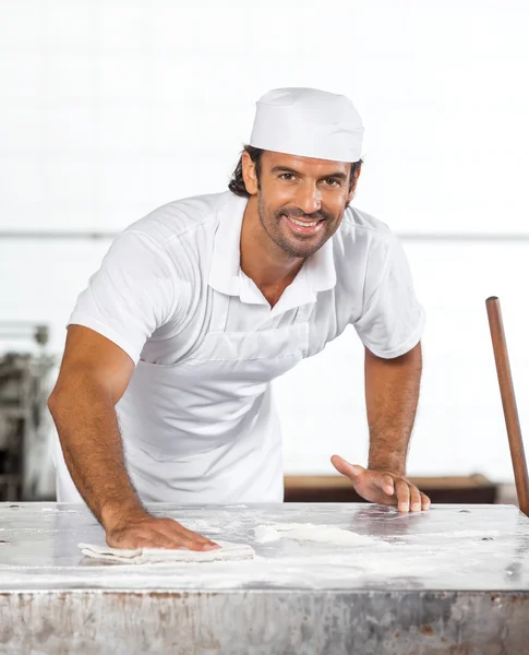 Selbstbewusster Bäcker putzt Mehl vom Tisch — Stockfoto