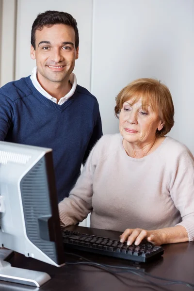 Glad lärare hjälpa äldre kvinna att använda dator — Stockfoto