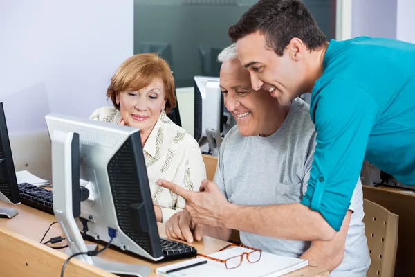 Tutor Assisting Senior Students In Using Computer At Class — Stock Photo, Image