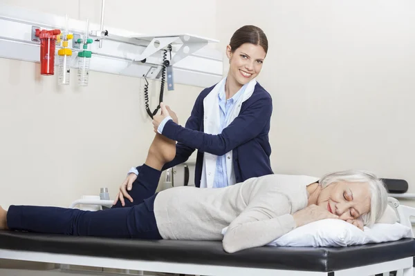 Feliz fisioterapeuta ayudando a la mujer mayor con ejercicio de la pierna —  Fotos de Stock