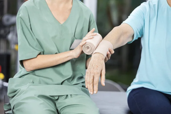 Infermiera femminile che mette fasciatura crespo sulla mano delle donne anziane — Foto Stock