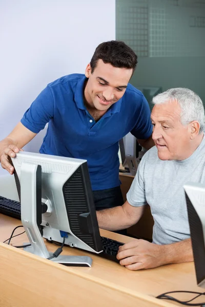 Teacher Assisting Senior Man In Using Computer At Classroom — Stock Photo, Image