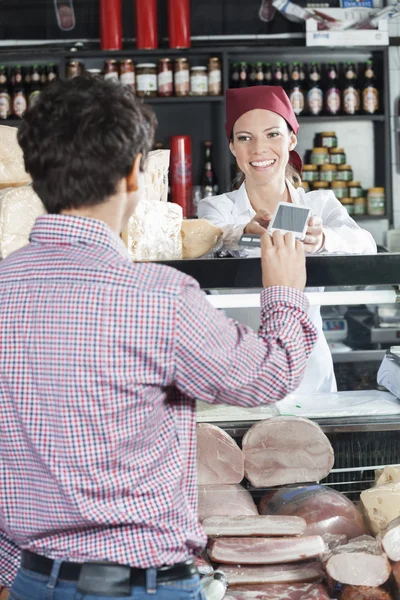 Продавец принимает платежи от клиента в сырном магазине — стоковое фото