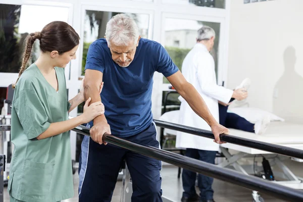 Physiotherapeutin steht Patientin beim Gehen zwischen parallelen — Stockfoto