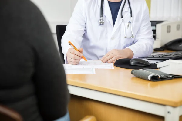 Midsection Of Doctor Writing Prescription For Patient At Desk — Stock Photo, Image