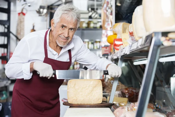 幸せなセールスマンのショップにナイフでチーズをスライスします。 — ストック写真