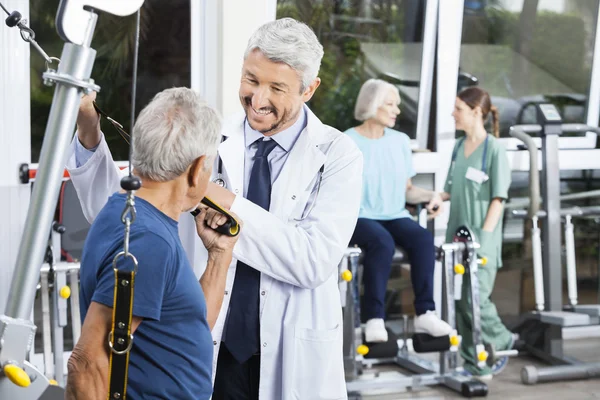 Happy doktor pomáhat starší muž s kapelou odpor — Stock fotografie