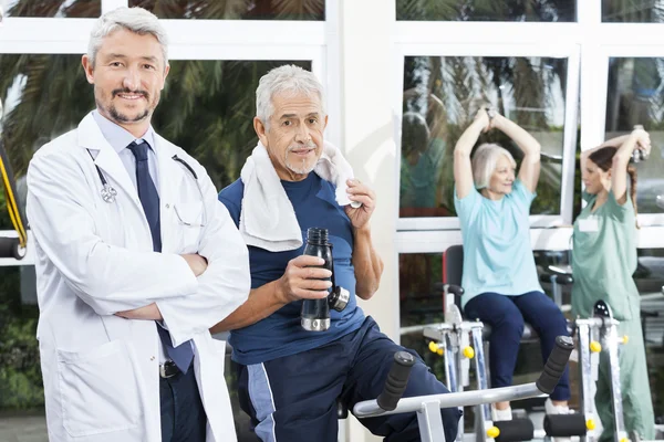 Уверенный пожилой человек и доктор в фитнес-студии — стоковое фото