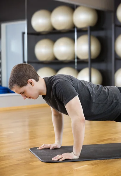 Hombre realizando flexiones en estera en el gimnasio —  Fotos de Stock