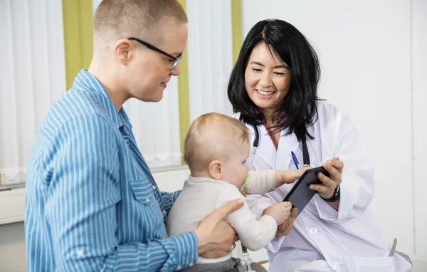 Mulher olhando para bebê agarrando tablet digital do médico feminino — Fotografia de Stock