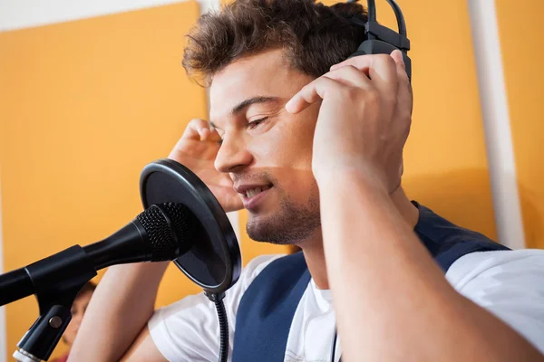 Cantor ajustando fones de ouvido enquanto canta no estúdio de gravação — Fotografia de Stock