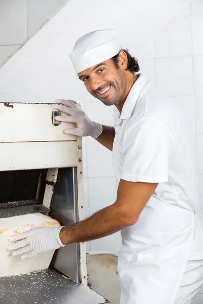 Orta yetişkin erkek Baker ekmek dilimleme makinesi kullanarak gülümseyen — Stok fotoğraf