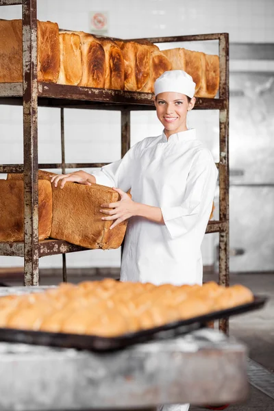 Joven hembra panadero quitar pan pan de rack —  Fotos de Stock