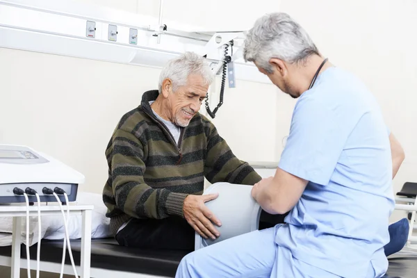 Fysiotherapeut onderzoekt Senior patiënt op Bed — Stockfoto