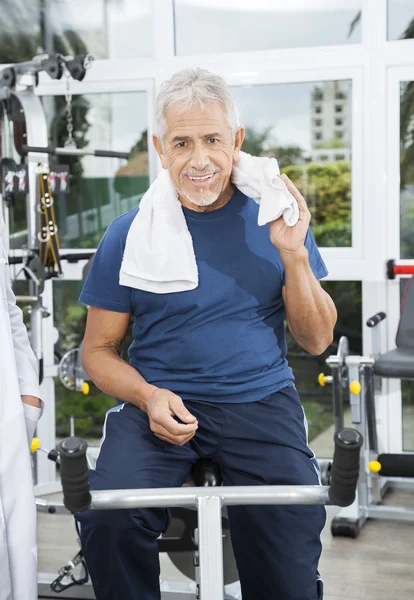 Homem sênior sentado em bicicleta de exercício no centro de fitness de reabilitação — Fotografia de Stock