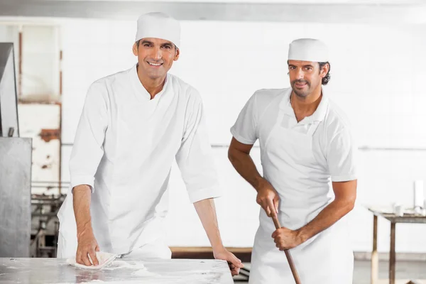 Los panaderos masculinos sonriendo mientras limpian la panadería — Foto de Stock